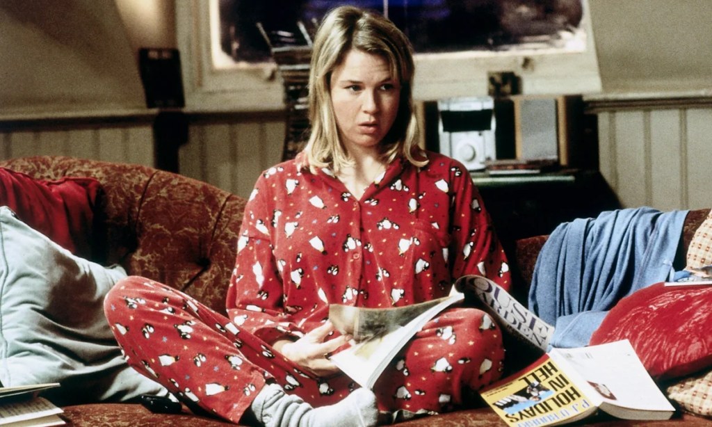 Renée Zellweger in red pyjamas, sitting cross-legged on a sofa with a magazine.