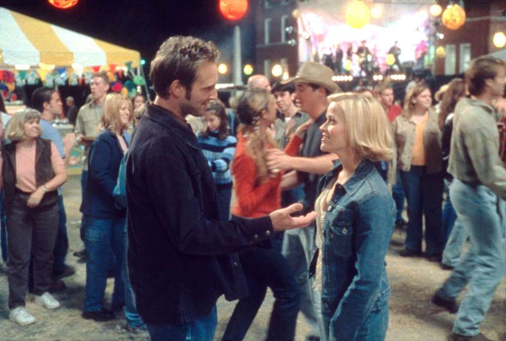 Josh Lucas and Reese Witherspoon talking in the middle of a crowded small-town fair at night.