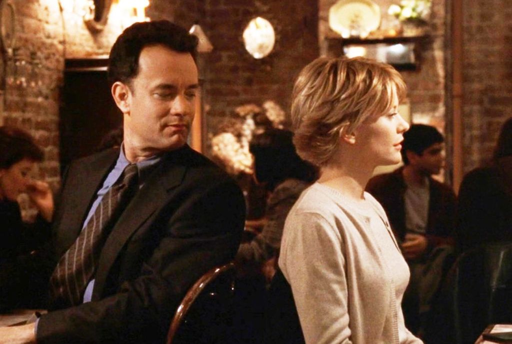 Tom Hanks and Meg Ryan sitting in a busy, warmly lit café.
