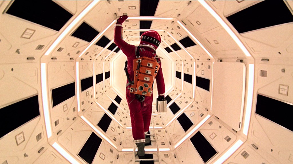 An astronaut in a red spacesuit climbing through a white, octagonal corridor, a scene from 2001: A Space Odyssey.