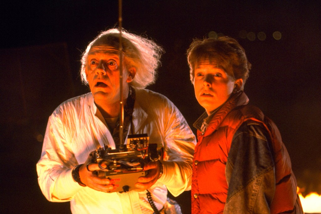 Christopher Lloyd holding a remote control next to Michael J. Fox in a red puffer vest, both looking shocked at night, in Back to the Future.
