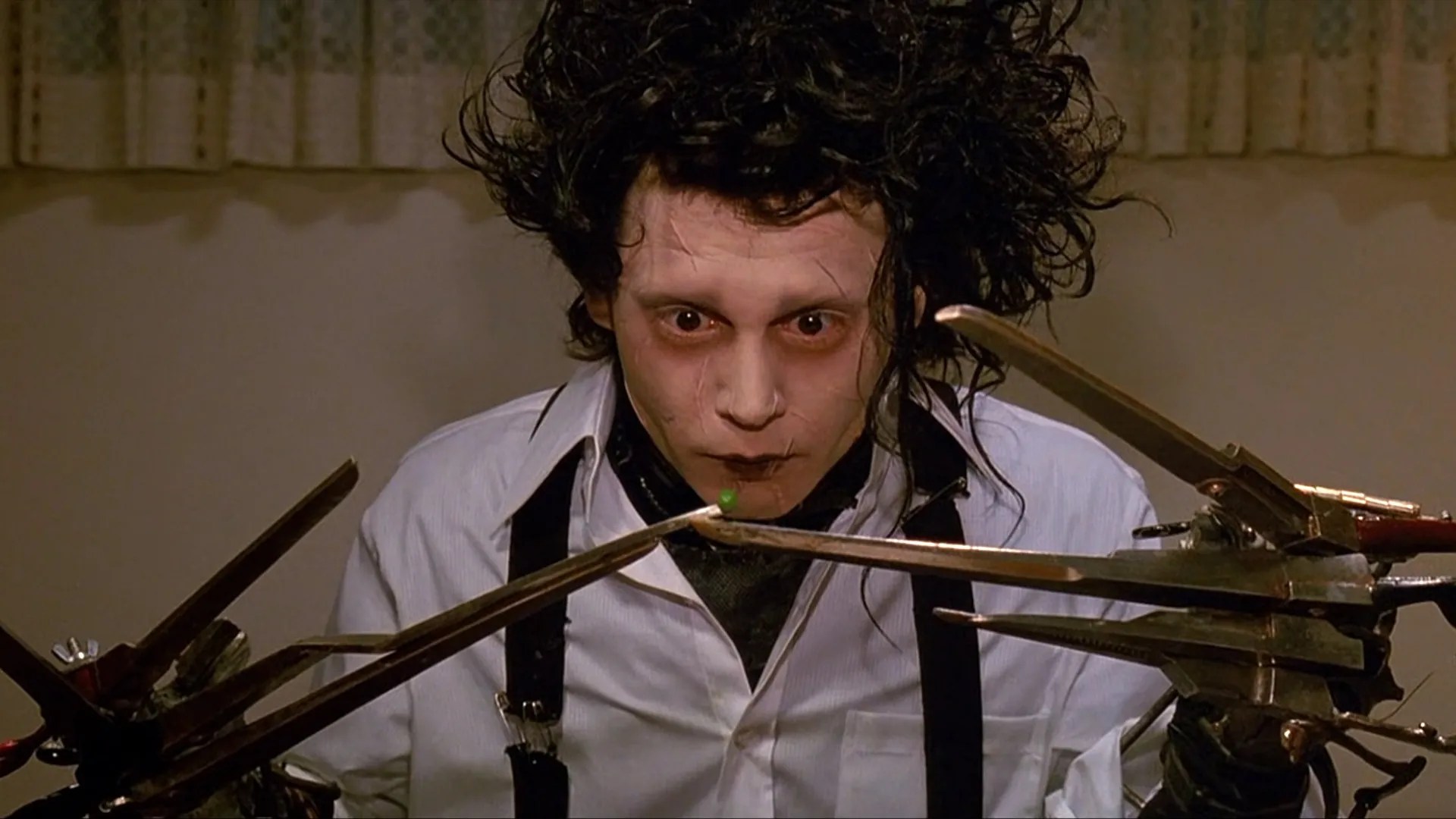 Johnny Depp as Edward, with wild black hair and pale skin, balancing a single pea on the tip of his scissor blades at the dinner table in Edward Scissorhands.