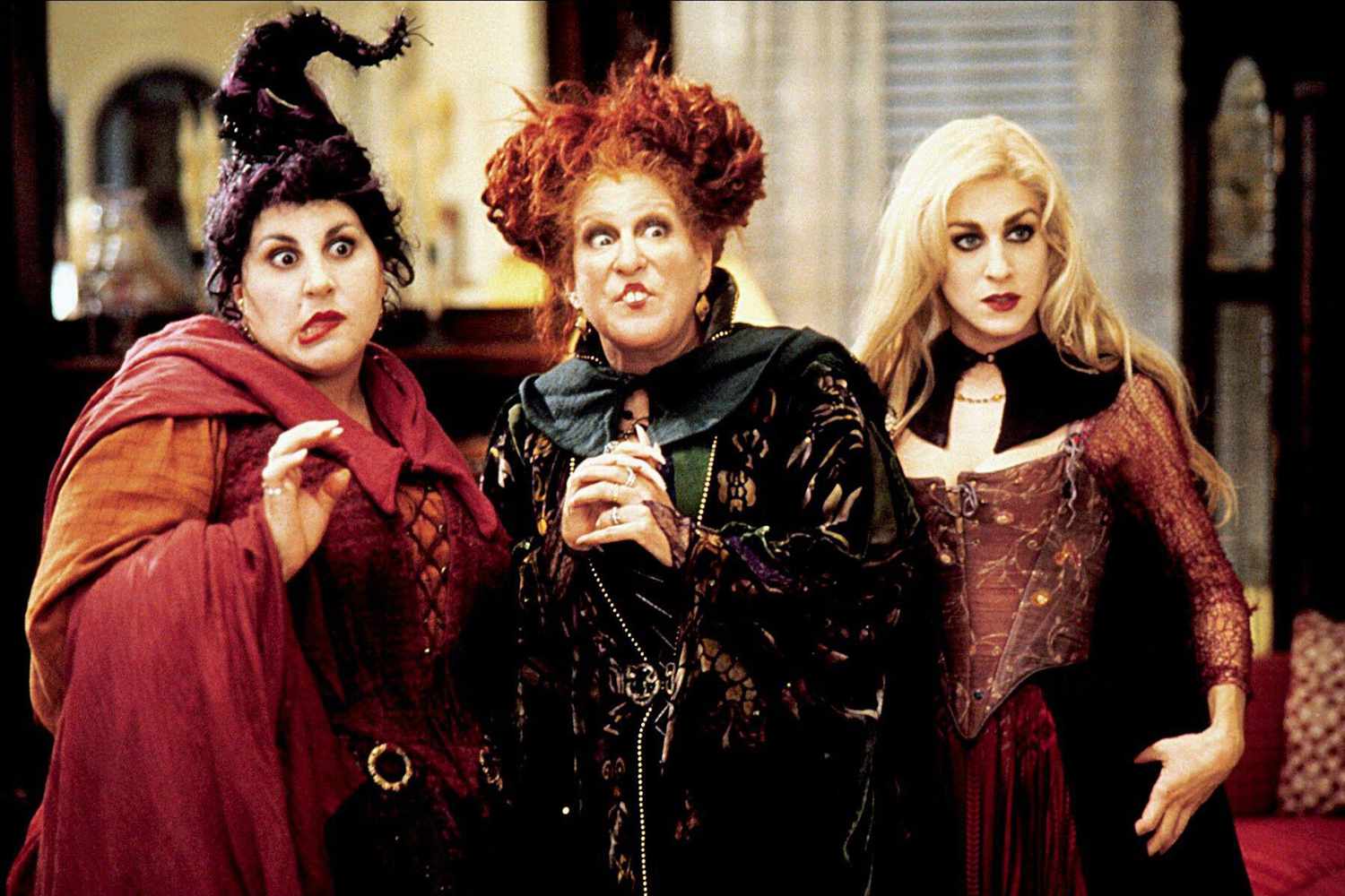 Kathy Najimy, Bette Midler and Sarah Jessica Parker as the three Sanderson sisters in their witch costumes, pulling faces in a living room in Hocus Pocus.