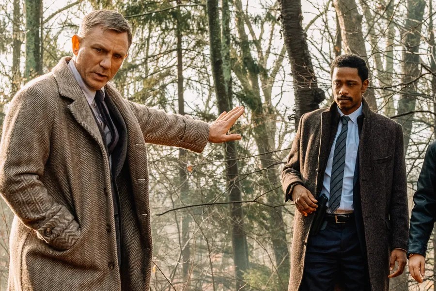 Daniel Craig in a tweed coat gesturing in a bare autumn forest, with LaKeith Stanfield standing beside him, in Knives Out.