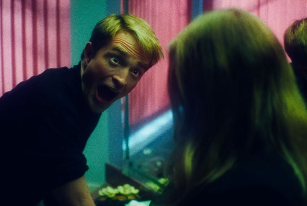 Chris Hansen leans in with wide eyes and an open-mouthed shout at a woman seen from behind, in a room lit pink and green, from the film "Primetime".