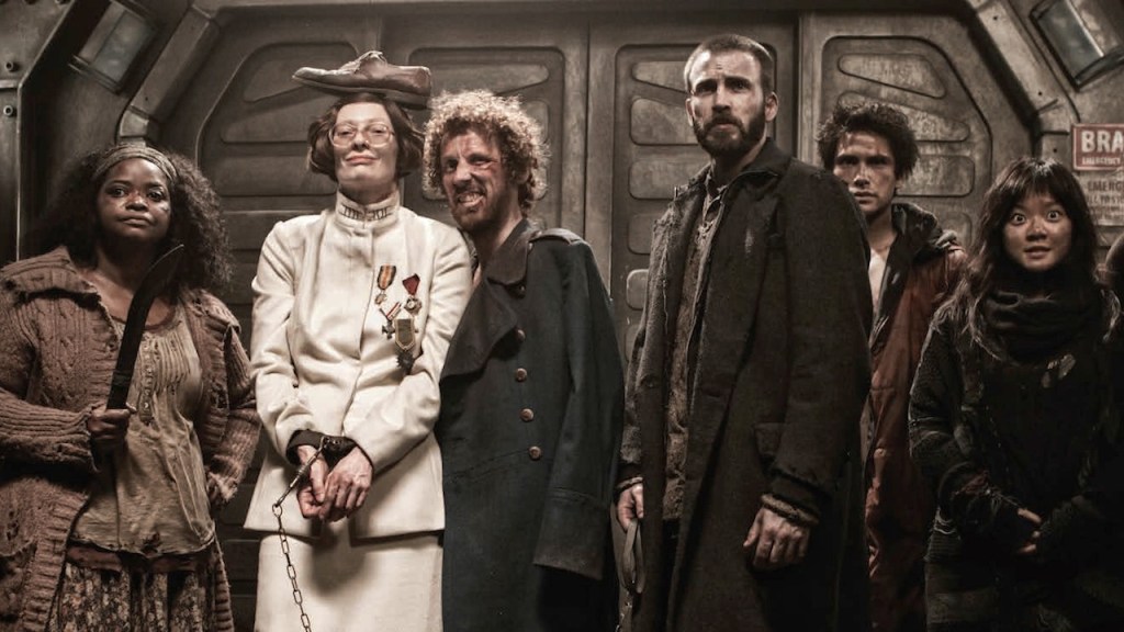 The cast of Snowpiercer lined up inside the train, with Tilda Swinton wearing a shoe on her head.